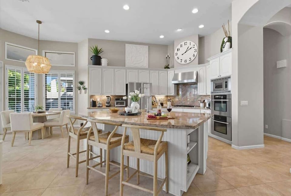 The kitchen showcases granite countertops, crisp white cabinets, stainless steel appliances, and a spacious island with breakfast bar seating for three.