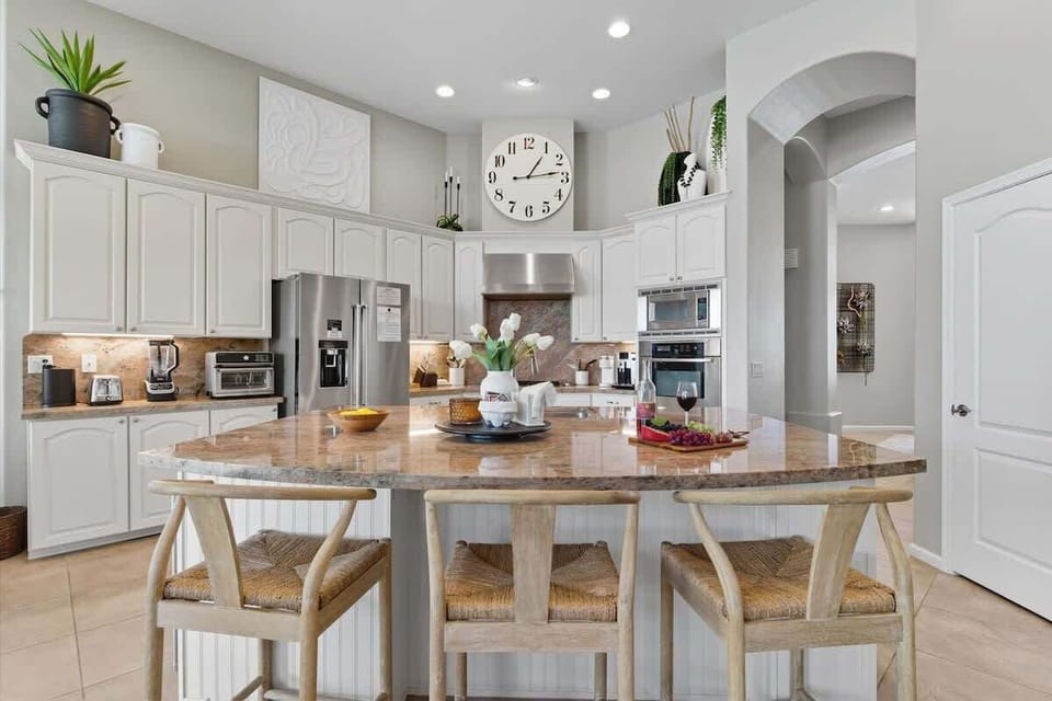The kitchen showcases granite countertops, crisp white cabinets, stainless steel appliances, and a spacious island with breakfast bar seating for three.