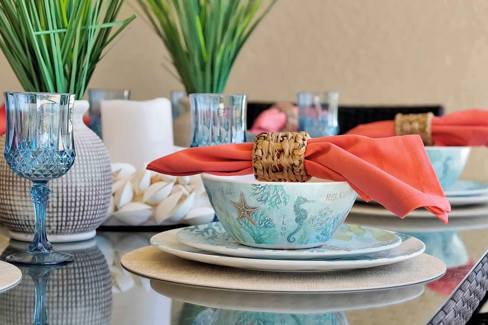 Coastal-themed table setting with coral-colored napkins and blue glassware for a relaxing dining experience.