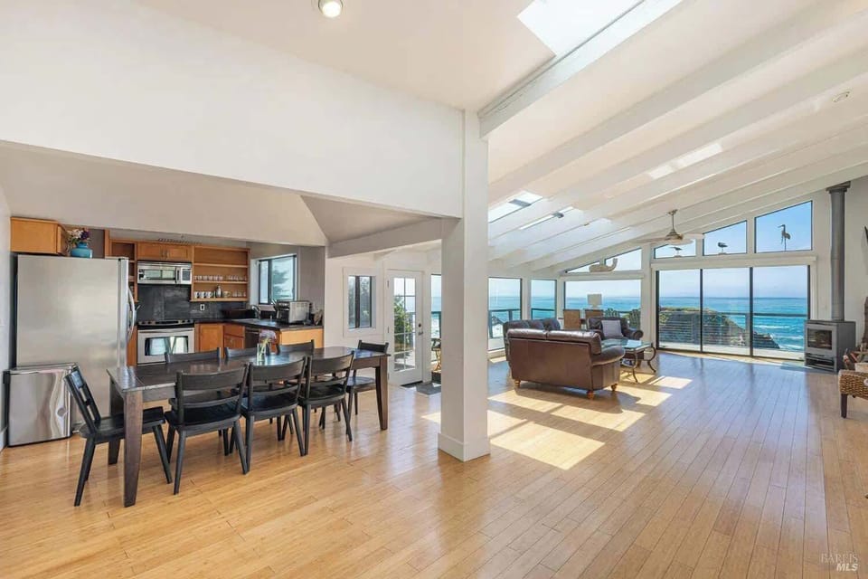This inviting space blends the kitchen, dining table, and sunny living room. Enjoy easy meals, warm light, and stunning coastal scenery from every corner.
