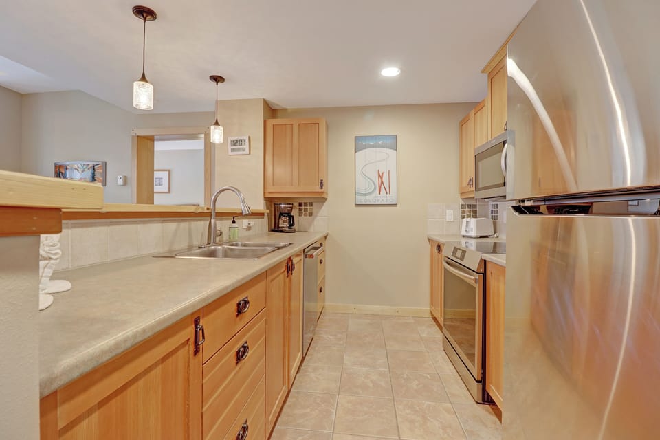 Bright and functional full kitchen featuring warm wood cabinetry, stainless steel appliances, and generous counter space—perfect for preparing meals before or after mountain adventures.
