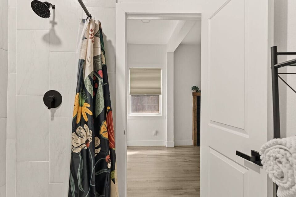 This ensuite bathroom features a clean tile shower with matte black fixtures and a bold, colorful curtain to brighten your morning routine.