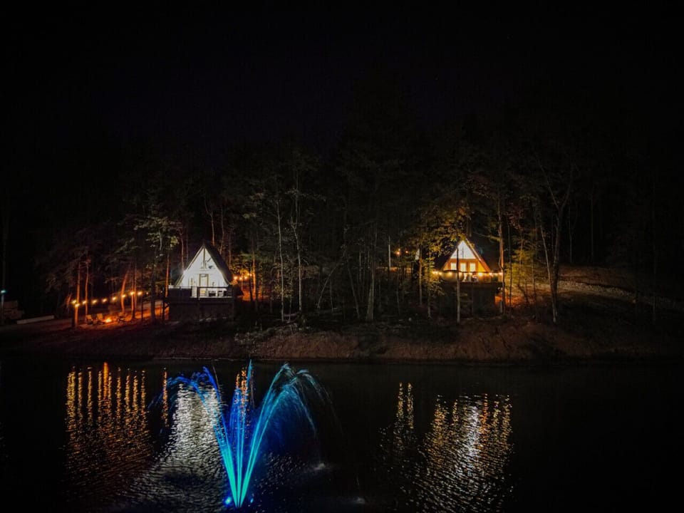 Twinkling cabin lights and a glowing fountain create a magical lakeside atmosphere at night. ✨🌙