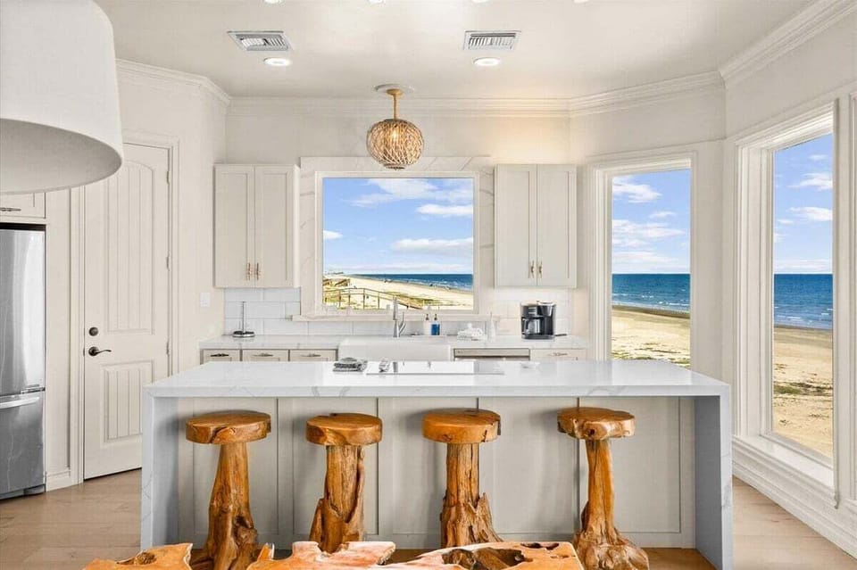 With unobstructed ocean views from every angle, the chef's kitchen is a showpiece of coastal sophistication — complete with a gleaming waterfall island and handcrafted wooden barstools that echo the natural beauty beyond.