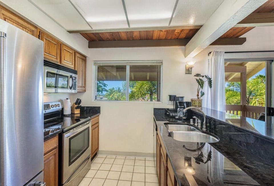Galley kitchen with full appliances and ocean glimpses through windows.