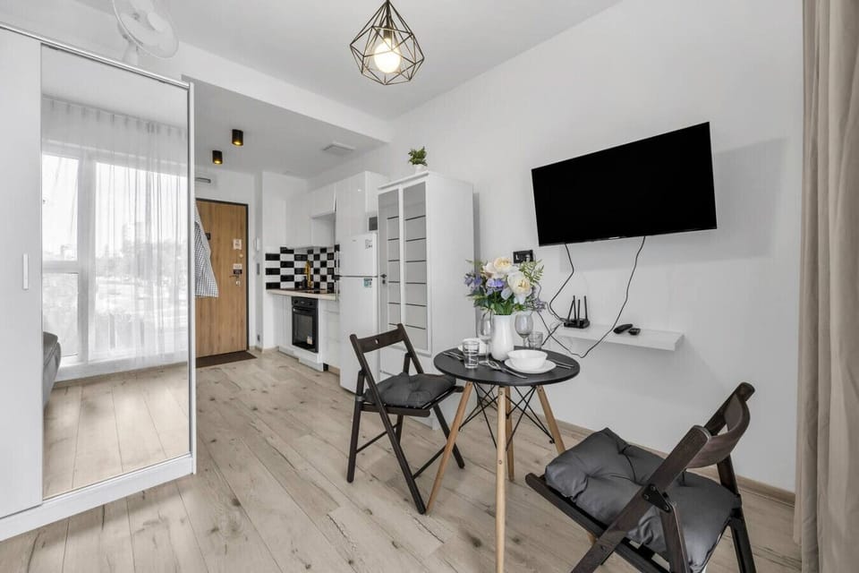 Main Living & Sleeping Area – Comfortable fold-out sofa that converts into a bed, stylish dining table setup, flat-screen TV and bright interiors with floor-to-ceiling curtains | Book Now with RENTUJEMY.COM