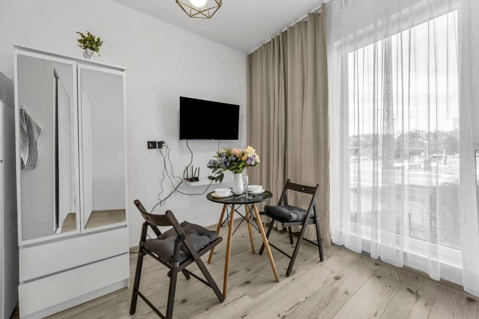 Main Living & Sleeping Area – Comfortable fold-out sofa that converts into a bed, stylish dining table setup, flat-screen TV and bright interiors with floor-to-ceiling curtains | Book Now with RENTUJEMY.COM