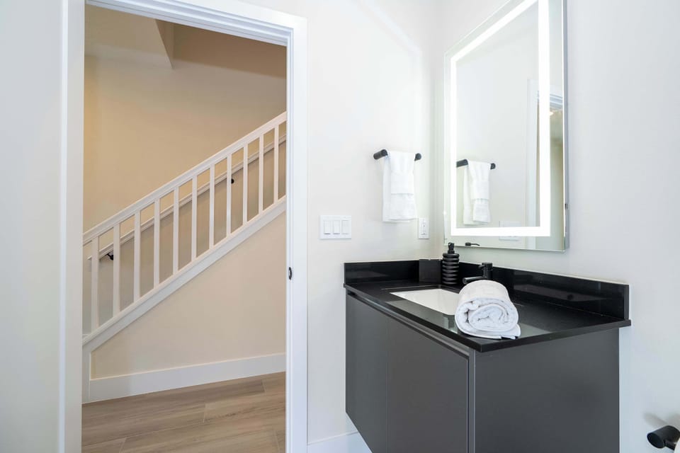This convenient half-bath features a sleek black vanity and a modern backlit mirror, located right off the main living area for easy access.