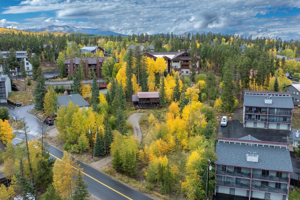 Aerial view of a mountain community showcasing vibrant autumn foliage and residential buildings nestled among colorful trees.