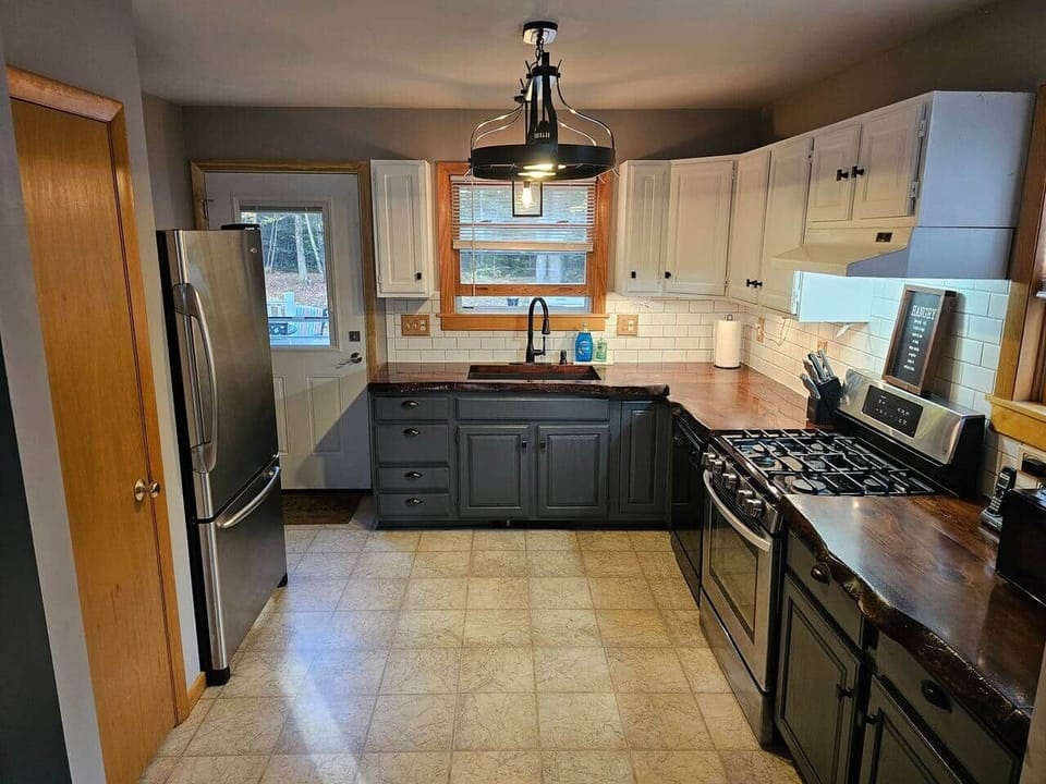 This stylish kitchen features two roomy pantry closets, stainless appliances, a 5-burner gas range, and a farmhouse sink. Wood counters and contrasting cabinetry create a rustic-modern space perfect for family meals.
