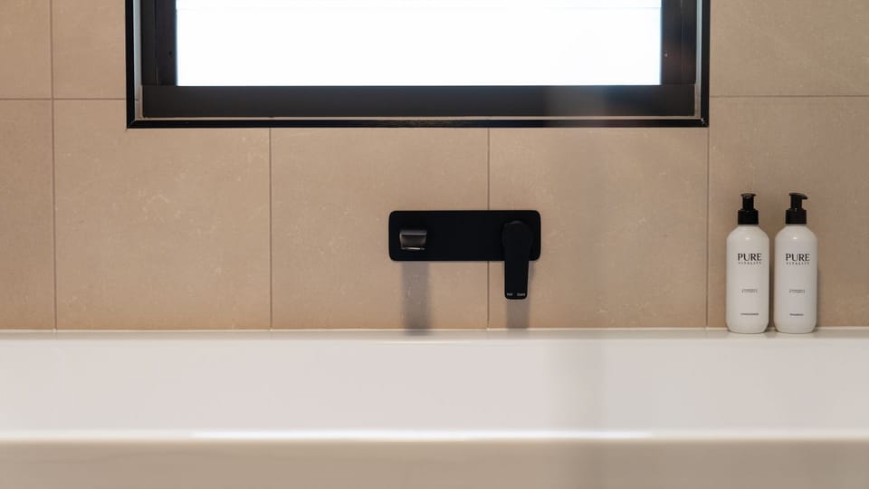 Minimalist bathtub setup with black hardware fixtures and sleek wall tiling.