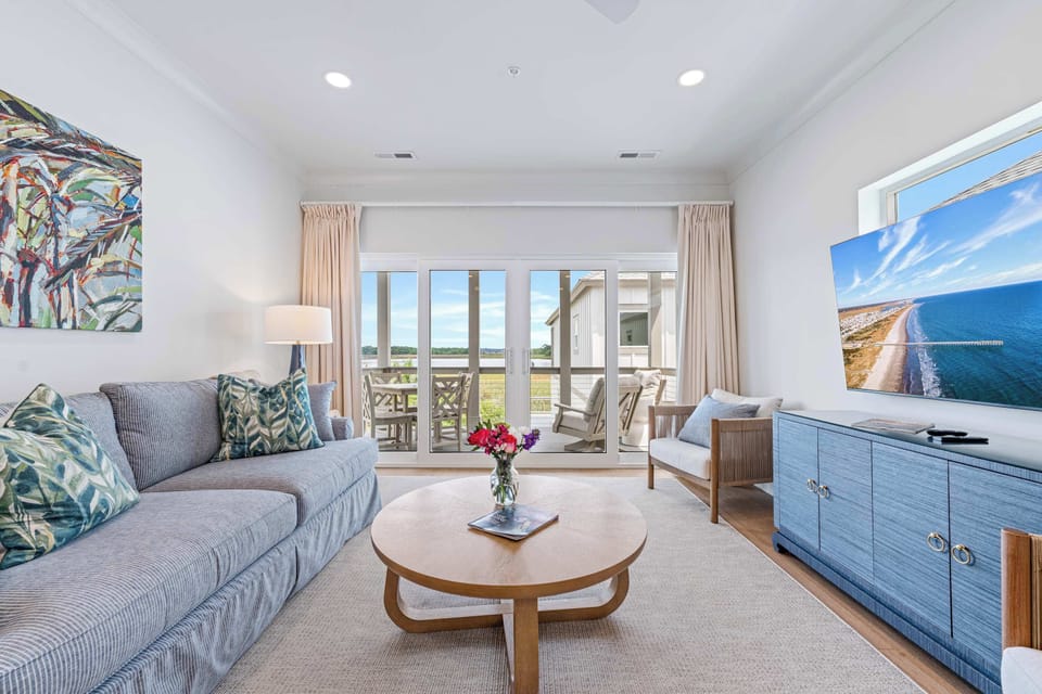 Relax in style as natural light fills this open living area, featuring plush seating with a pullout sofa, and direct access to a private balcony with sweeping marsh views.