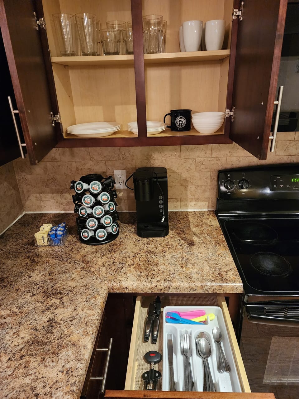 Kitchen has spoons, forks, kid utensils, glasses, plates and Keurig machine