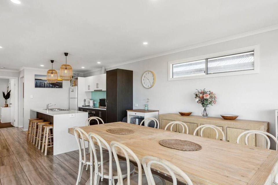 Gather around the dining table beneath rattan pendant lighting, where the open-plan layout flows seamlessly into the kitchen for shared meals and conversation.