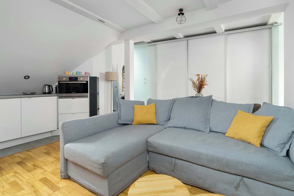 A sunlit lounge with a soft grey sofa, warm wooden floors, and minimalist decor creating a welcoming atmosphere.