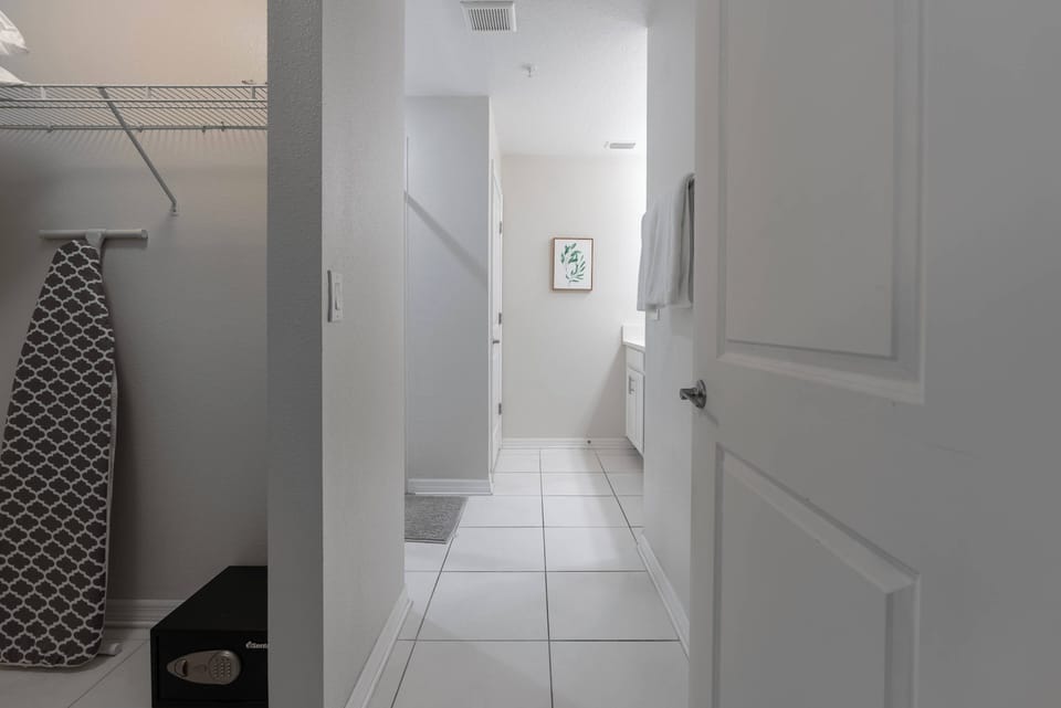 Step into a bright, airy hallway featuring sleek white tiles that reflect natural light, guiding you to a stylish bathroom and storage area. A touch of modern decor adds charm, creating an inviting first impression for your stay.