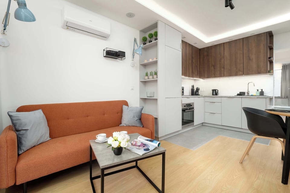 The kitchen and living area seen together, showing a harmonious and practical open-plan design. Light wood floors complement the white and wooden cabinetry.