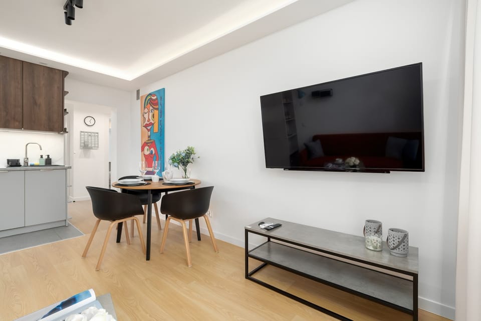 A modern living room with a large wall-mounted TV and a dining table. The neutral color palette enhances the sense of space and comfort.