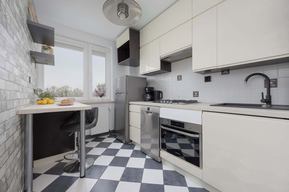 A compact kitchen with white cabinetry, grey tiled backsplash, and checkered flooring.