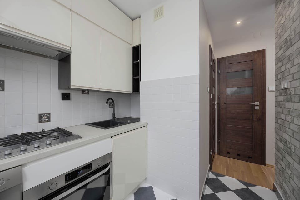 A galley kitchen showcasing stainless-steel appliances and modern grey brick-patterned tiles.