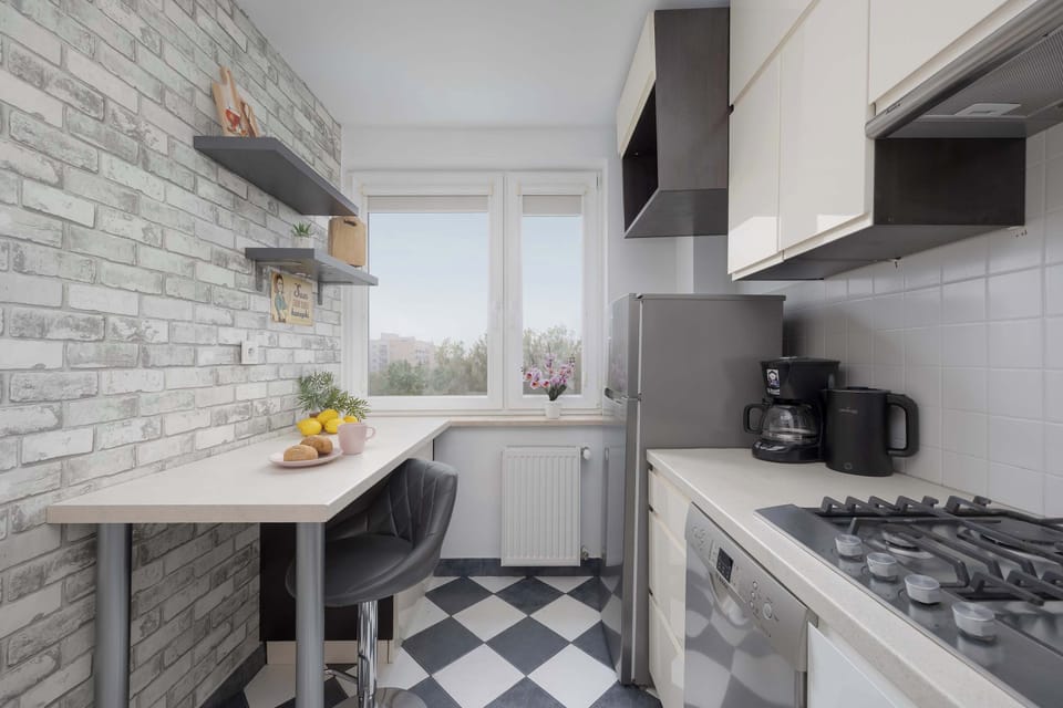A compact kitchen with white cabinetry, grey tiled backsplash, and checkered flooring.