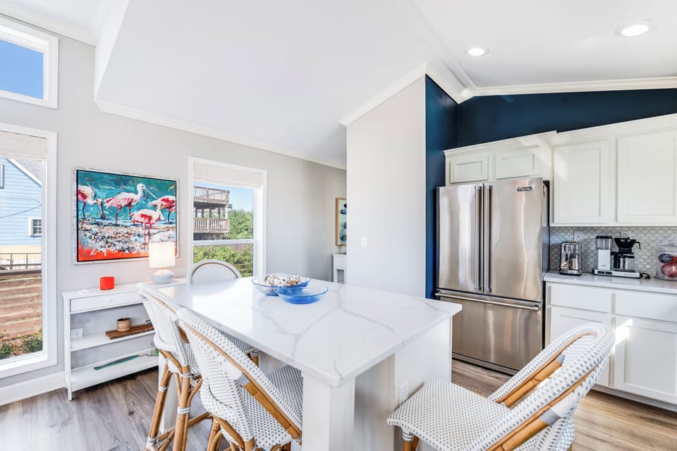 Gather around your bright, modern kitchen island where marble countertops and coastal charm create the perfect space for morning coffee and evening conversations.
