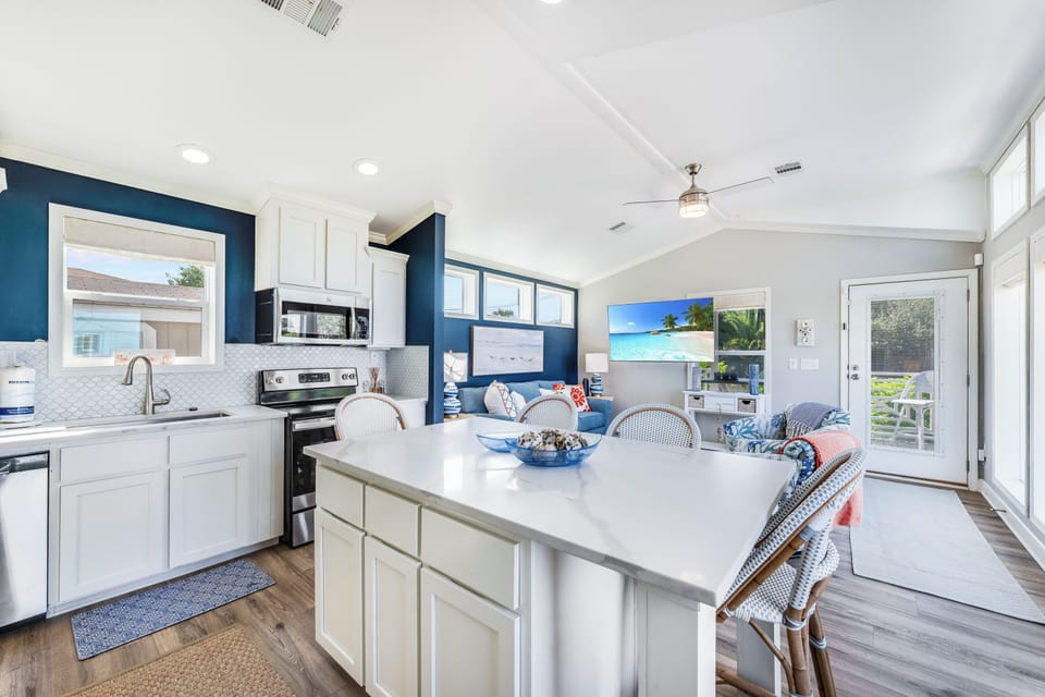Your bright open-concept space features a modern kitchen with white quartz counters flowing into a cozy living area, perfect for memorable vacation meals.