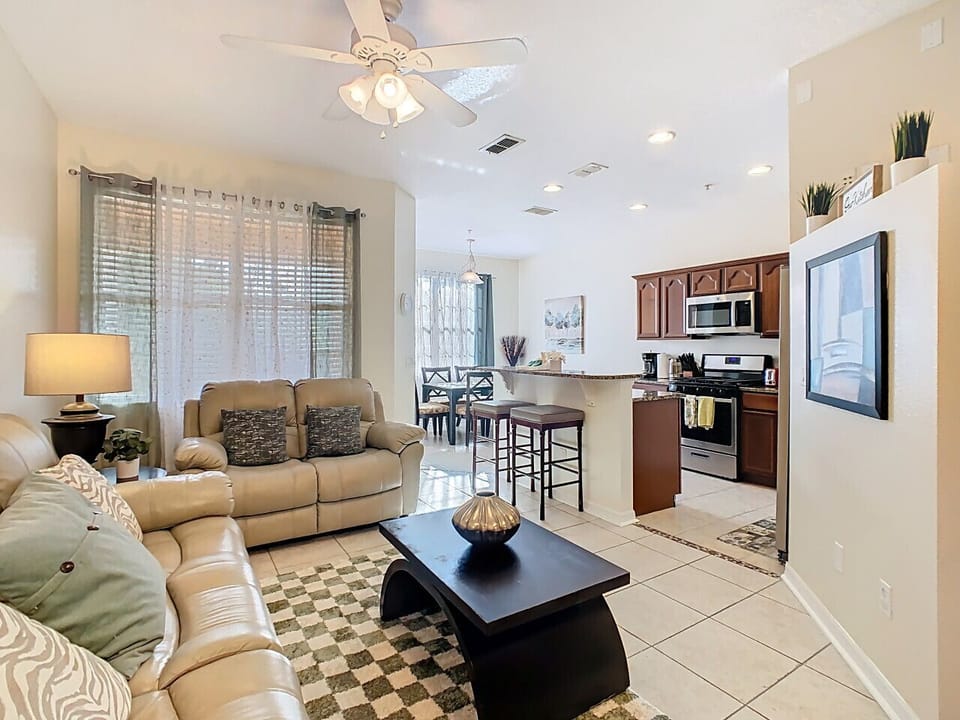 Open-concept living and kitchen area featuring plush sofas, large windows, and a fully equipped modern kitchen.