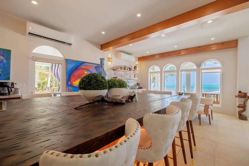 The kitchen island offers generous seating and serves as a central gathering place, with arched windows framing beautiful ocean views. Warm wood accents, modern lighting, and an open layout make this space ideal for casual meals and conversation.