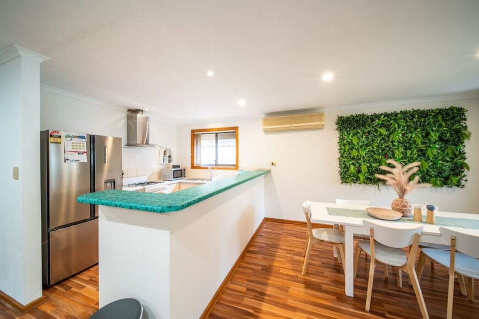Gather around the dining table beneath soft natural light, where the vibrant leafy feature wall adds a playful backdrop for long dinners and shared moments.