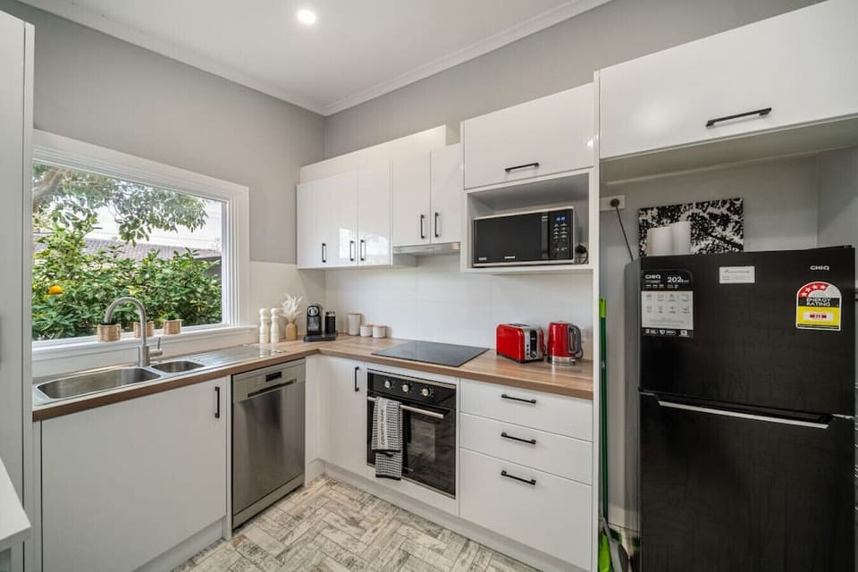Prepare meals with ease in the beautifully renovated kitchen featuring timber benchtops, a full-size fridge, induction cooktop, oven, microwave, toaster, kettle, and dishwasher—all surrounded by lush garden views.
