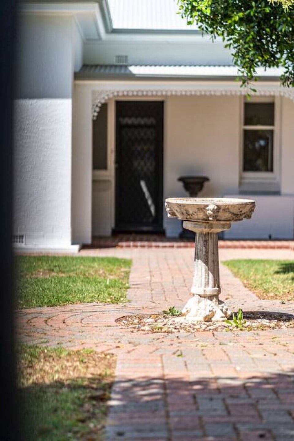 A classic brick pathway leads to the front door, with a rustic birdbath adding a touch of character to the garden.