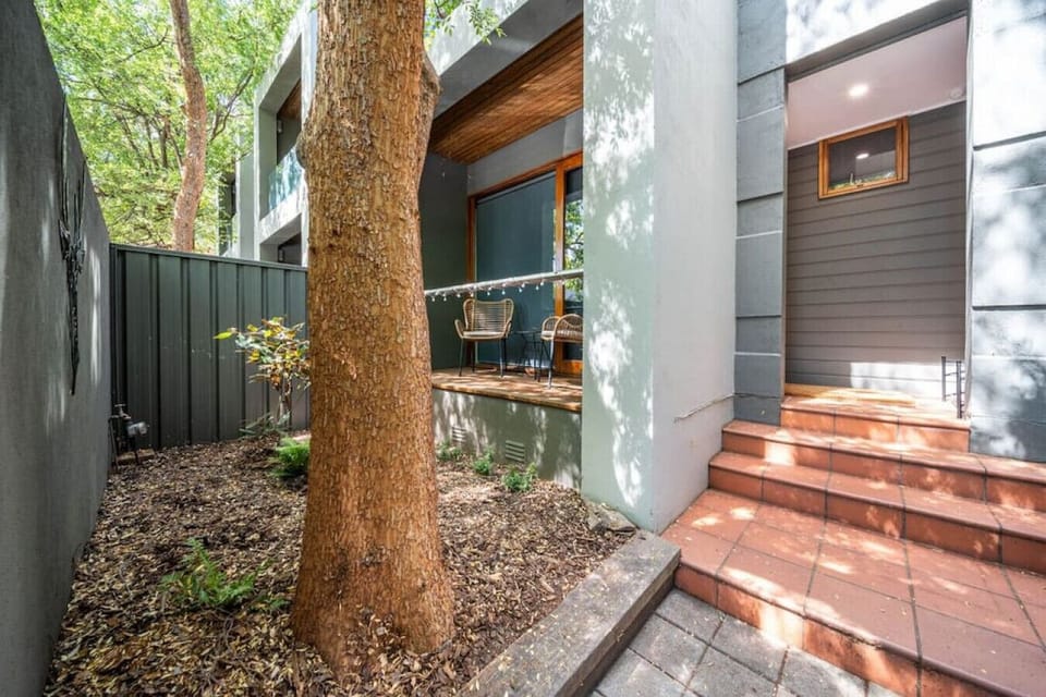 Step through the leafy entrance where mature trees and shaded seating create a calm welcome to the home.