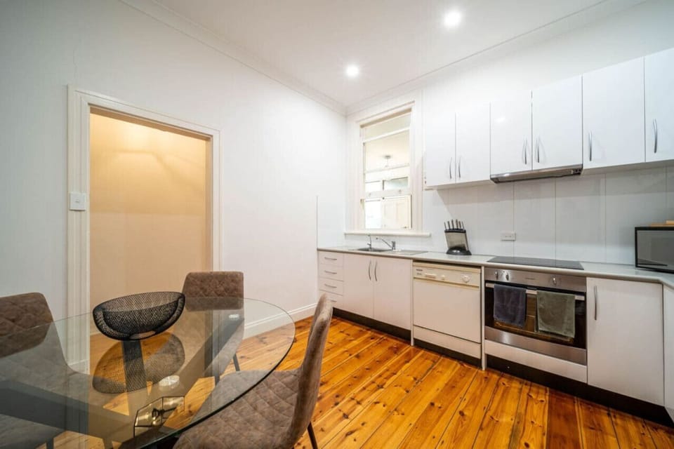 The kitchen features crisp white cabinetry, stainless steel appliances, and warm timber flooring.