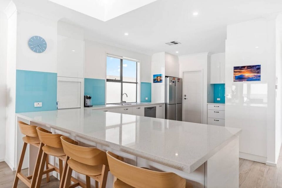 Cook with ease in the full kitchen, featuring sleek white cabinetry, sea-blue splashback accents, full-sized appliances, a coffee machine, and a spacious breakfast bar with stools.