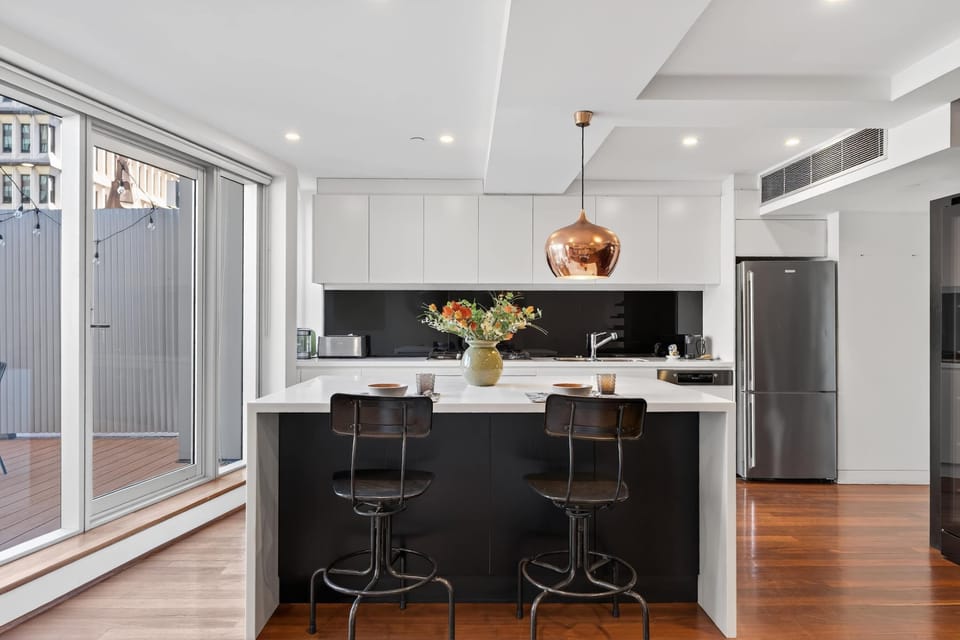 Stylish and fully equipped kitchen with premium appliances including an oven, dishwasher, cooktop, and coffee machine, complemented by a sleek counter table for two.