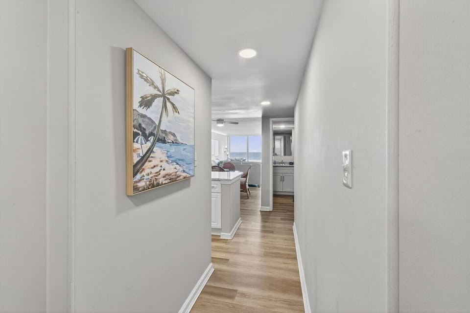 Bright hallway with coastal artwork leading into an open living space, offering a clear view of the ocean through large windows ahead.