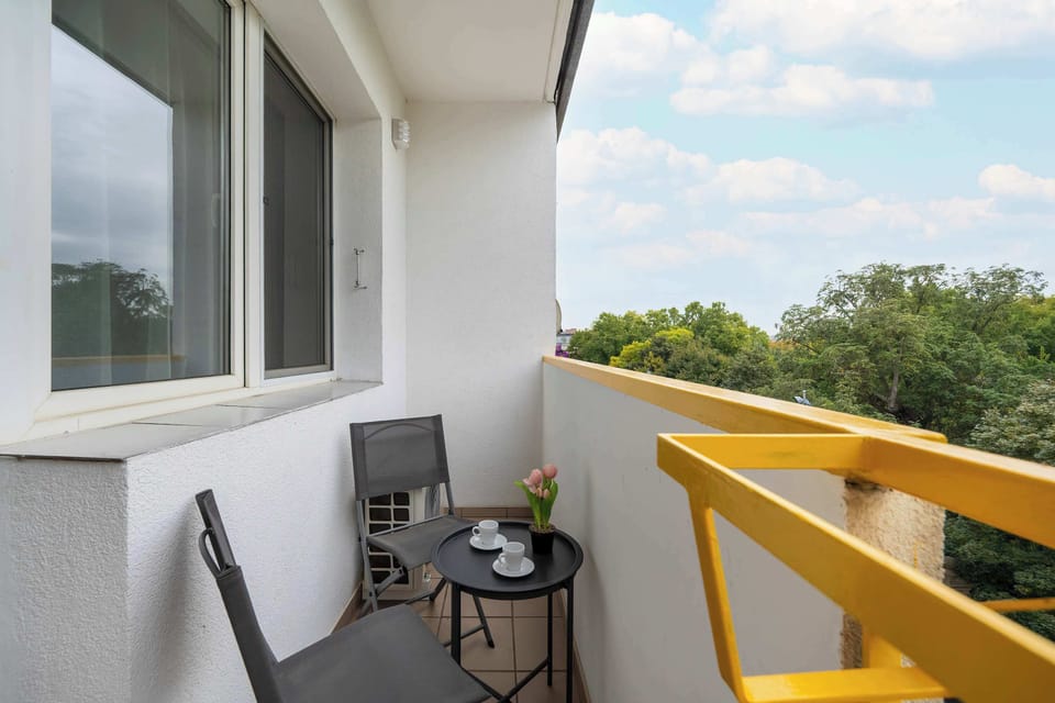 A small balcony with two chairs and a table overlooking the surrounding buildings.