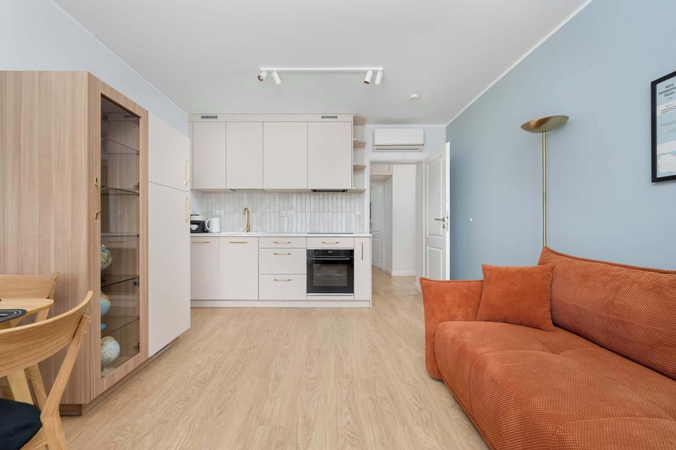 An open-plan kitchen and living room with light wood furniture and a welcoming orange sofa.