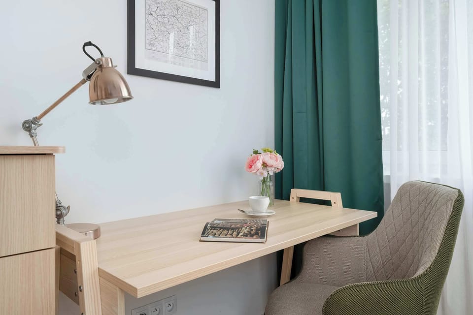 A simple writing desk with a lamp, framed art, and a vase of flowers on top.
