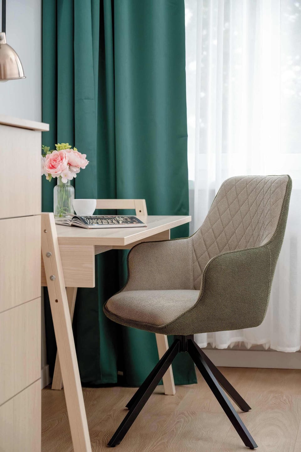 A small workspace with a wooden desk, beige chair, and natural light from the window.