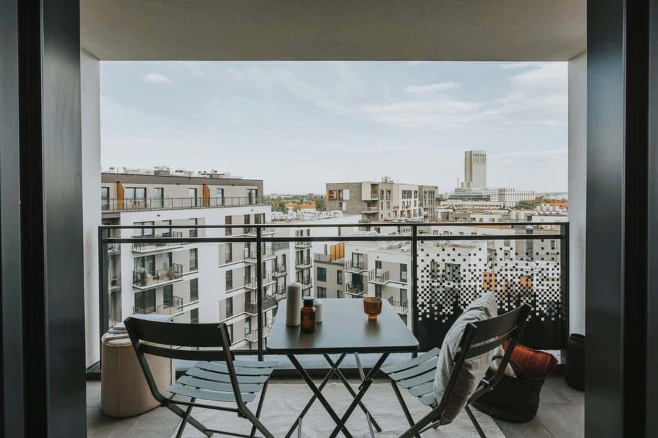 Balcony with a small seating area, perfect for enjoying coffee. Buildings in the distance add a city vibe.