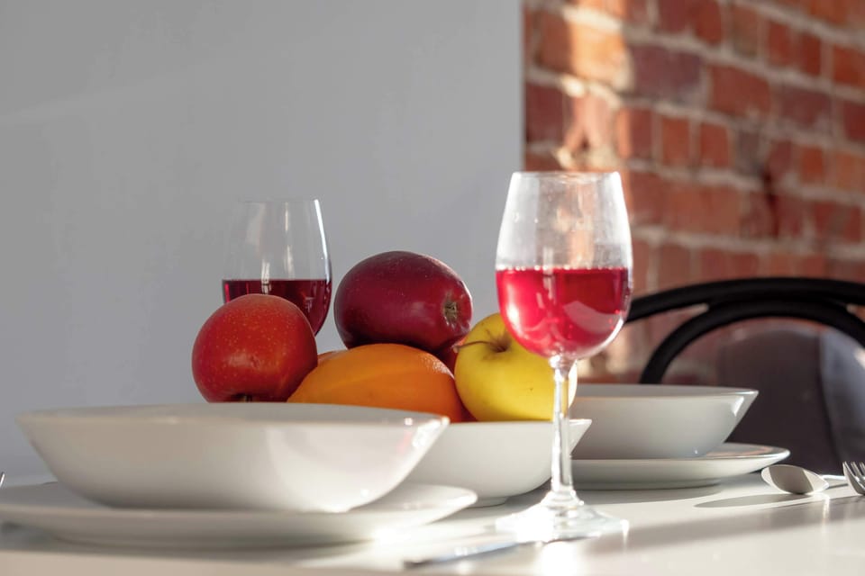 A small section of the kitchen countertop, showcasing a bowl of fresh fruit and two glasses of wine. The brick wall in the background adds a rustic touch to the modern kitchen.