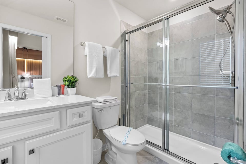 Experience the comfort of this stylish bathroom, featuring sleek gray tile and a spacious glass shower. The bright vanity area, complemented by fresh towels and a touch of greenery, creates a refreshing atmosphere for your stay.