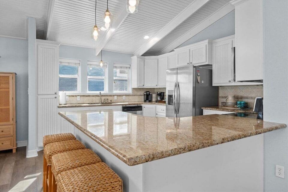 Modern kitchen with granite countertops, stainless steel appliances, and breakfast bar in this beach house rental.