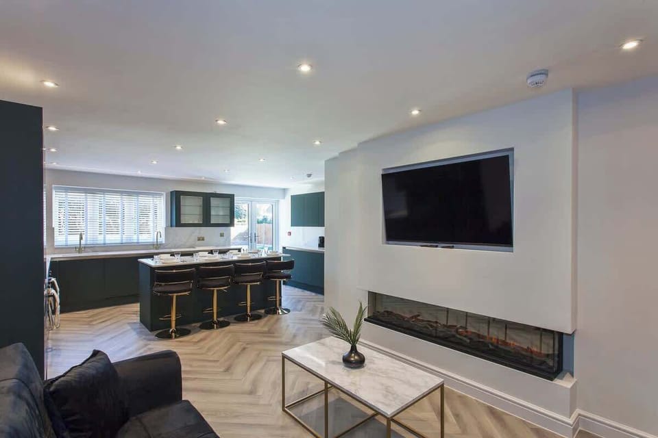Open-plan living and dining area with sleek kitchen, large Smart TV, and stylish electric fireplace — perfect for relaxing or entertaining.