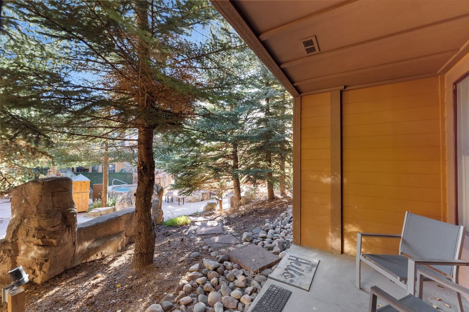Step onto your private covered patio where modern seating awaits beneath towering pines and natural stone accents.