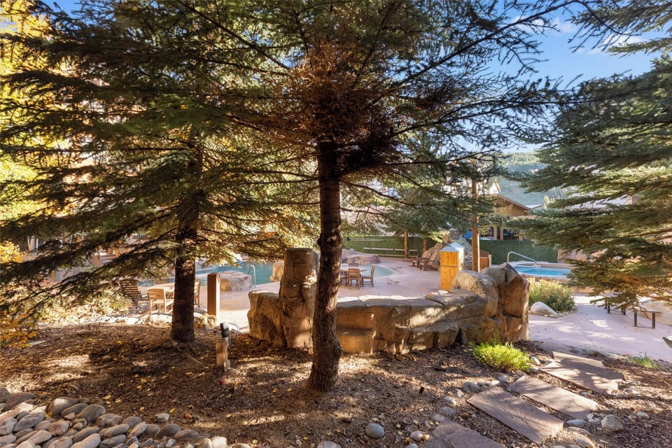 Relax beneath majestic pine trees where natural stone creates cozy seating areas overlooking the sparkling pool and mountain views.