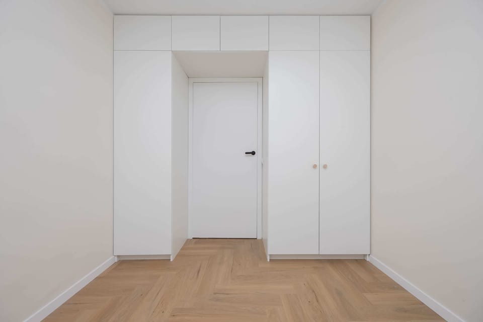 A minimalist hallway with white doors and wooden flooring for a clean, airy look.