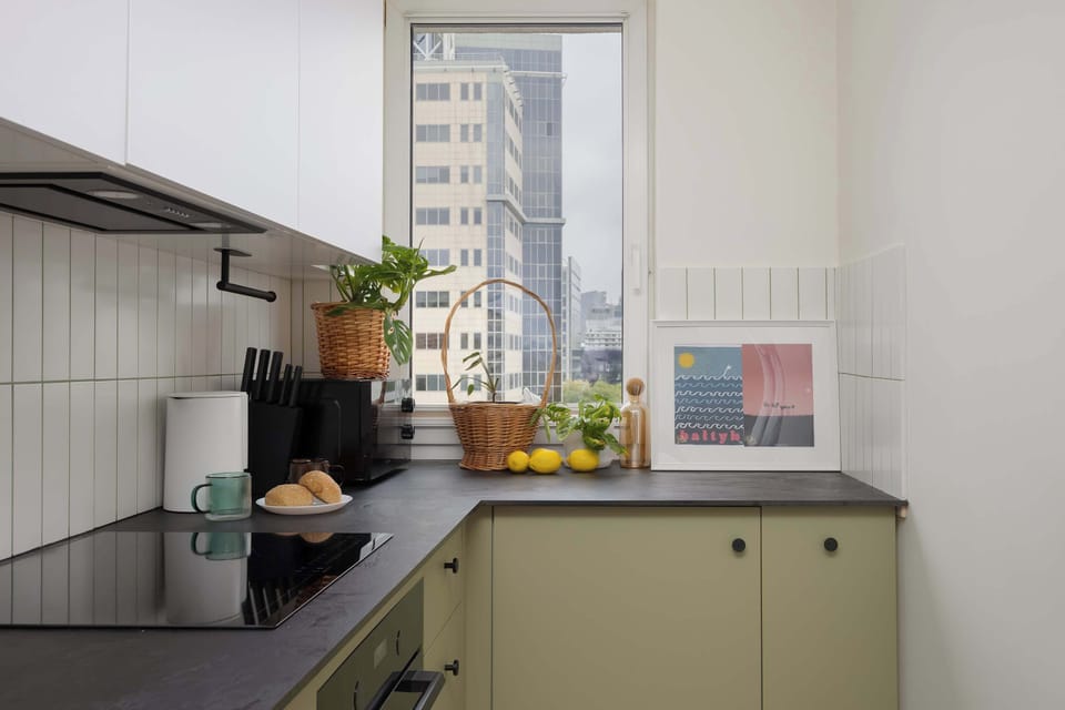 A stylish modern kitchen with green cabinets, a black countertop, and sleek built-in appliances.